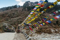 Le bandiere tibetane di preghiera fasciate con il ponte sopra il fiume congelato con la montagna nera con neve sulla cima è fondo Immagini Stock Libere da Diritti Le bandiere tibetane di preghiera fasciate con il ponte sopra il fiume congelato con la montagna nera con neve sulla cima è fondo Immagini Stock Libere da Diritti
