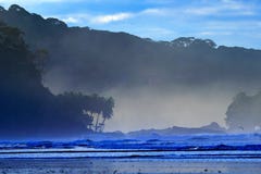 Le caillou et la plage sablonneuse pendant le lever de soleil, avec les vagues bleu-foncé et les nuages oranges, Se de crépuscule photo libre de droits Le caillou et la plage sablonneuse pendant le lever de soleil, avec les vagues bleu-foncé et les nuages oranges, Se de crépuscule photo libre de droits