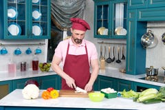 Le chef dans le tablier rouge coupe des légumes par le couteau en céramique sur la planche à découper images libres de droits Le chef dans le tablier rouge coupe des légumes par le couteau en céramique sur la planche à découper images libres de droits
