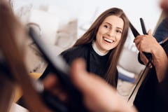 Le coiffeur féminin redressent les cheveux bruns à la femme employant le fer de cheveux dans le salon de beauté images stock Le coiffeur féminin redressent les cheveux bruns à la femme employant le fer de cheveux dans le salon de beauté images stock