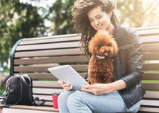 Le den unga kvinnan med minnestavlan och den lilla hunden på staden parkera arkivbilder Le den unga kvinnan med minnestavlan och den lilla hunden på staden parkera arkivbilder