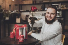 Le den unga mannen som sitter tabellen som rymmer en ros royaltyfri foto Le den unga mannen som sitter tabellen som rymmer en ros royaltyfri foto