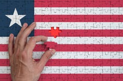 Le drapeau du Libéria est dépeint sur un puzzle, que la main du ` s d'homme accomplit pour plier images stock Le drapeau du Libéria est dépeint sur un puzzle, que la main du ` s d'homme accomplit pour plier images stock