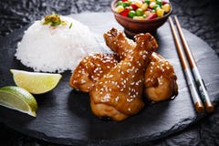 Le gambe di pollo fritto con il teriyaki sauce i semi di sesamo ed il riso sulla pietra nera Fotografia Stock Le gambe di pollo fritto con il teriyaki sauce i semi di sesamo ed il riso sulla pietra nera Fotografia Stock