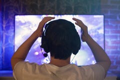 Le Gamer ou la flamme dans des écouteurs avec le microphone s'assied à la maison dans la chambre noire et joue avec des amis sur photographie stock libre de droits Le Gamer ou la flamme dans des écouteurs avec le microphone s'assied à la maison dans la chambre noire et joue avec des amis sur photographie stock libre de droits