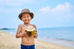 Le garçon asiatique bronzé se tient sur la plage dans un chapeau et une noix de coco de boissons images libres de droits Le garçon asiatique bronzé se tient sur la plage dans un chapeau et une noix de coco de boissons images libres de droits