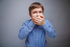 Le garçon dans une chemise a couvert la bouche d'effroi de ses mains photo libre de droits Le garçon dans une chemise a couvert la bouche d'effroi de ses mains photo libre de droits