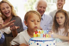 Le garçon souffle des bougies de gâteau d'anniversaire à la partie de famille image stock Le garçon souffle des bougies de gâteau d'anniversaire à la partie de famille image stock