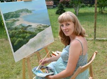 Le jeune artiste féminin enceinte peint un tableau, se reposant à un chevalet images stock Le jeune artiste féminin enceinte peint un tableau, se reposant à un chevalet images stock