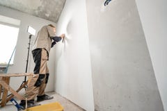 Le jeune dépanneur aligne avec la spatule en plastique Travailleur collant des papiers peints sur le mur en béton R?parez l'appar photo libre de droits Le jeune dépanneur aligne avec la spatule en plastique Travailleur collant des papiers peints sur le mur en béton R?parez l'appar photo libre de droits