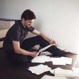 Le jeune entrepreneur masculin fait la séance de réflexion se reposant sur le plancher dans l'appartement Approche créative aux a images libres de droits Le jeune entrepreneur masculin fait la séance de réflexion se reposant sur le plancher dans l'appartement Approche créative aux a images libres de droits