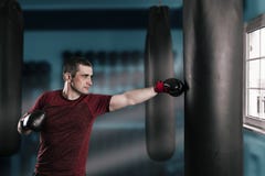 Le jeune homme aux cheveux courts s'exerce dans un gymnase avec un sac de sable image stock Le jeune homme aux cheveux courts s'exerce dans un gymnase avec un sac de sable image stock