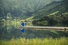 Le jeune homme dans le pull molletonné bleu se tient sur le pilier à côté du lac volcanique photos stock Le jeune homme dans le pull molletonné bleu se tient sur le pilier à côté du lac volcanique photos stock
