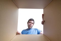 Le jeune homme déçu regarde sur le cadeau à l'intérieur de la boîte en carton image libre de droits Le jeune homme déçu regarde sur le cadeau à l'intérieur de la boîte en carton image libre de droits