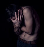 Le jeune homme musculaire sexy s'est blotti dans une boule sur le fond foncé du côté avec remet son visage photo stock Le jeune homme musculaire sexy s'est blotti dans une boule sur le fond foncé du côté avec remet son visage photo stock