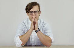 Le jeune mâle sérieux même caucasien dans la robe longue blanche repose le froncement de sourcils, mains sur la table Regard de s photos libres de droits Le jeune mâle sérieux même caucasien dans la robe longue blanche repose le froncement de sourcils, mains sur la table Regard de s photos libres de droits