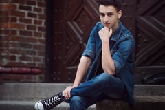 Le jeune type en denim, promenades sur la rue, s'asseyent photographie stock Le jeune type en denim, promenades sur la rue, s'asseyent photographie stock