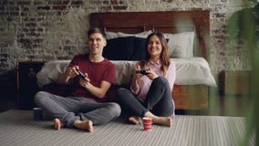 Le jeunes ami et amie mignons de couples jouent le jeu vidéo tenant des manettes se reposant sur le plancher de chambre à coucher banque de vidéos Le jeunes ami et amie mignons de couples jouent le jeu vidéo tenant des manettes se reposant sur le plancher de chambre à coucher banque de vidéos