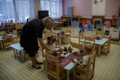 Le Kindergartener aide des enfants à manger Peu garçon et fille mangeant le petit déjeuner au jardin d'enfants images stock Le Kindergartener aide des enfants à manger Peu garçon et fille mangeant le petit déjeuner au jardin d'enfants images stock