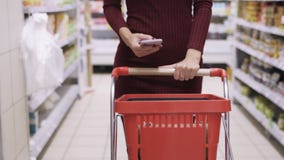 Le mani della donna del primo piano rotolano il carretto rosso nel pavimento di commercio del supermercato e del telefono di uso stock footage Le mani della donna del primo piano rotolano il carretto rosso nel pavimento di commercio del supermercato e del telefono di uso stock footage