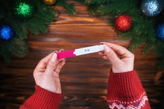 Le mani femminili mette la tenuta del test di gravidanza come regalo di Natale Tavola di legno con le decorazioni del nuovo anno immagine stock libera da diritti Le mani femminili mette la tenuta del test di gravidanza come regalo di Natale Tavola di legno con le decorazioni del nuovo anno immagine stock libera da diritti