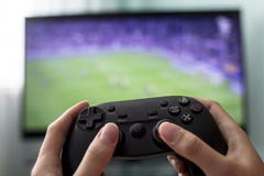 Le mani femminili tengono la leva di comando sui precedenti della TV, un gioco di calcio, il primo piano, una ragazza un gamer fotografie stock libere da diritti Le mani femminili tengono la leva di comando sui precedenti della TV, un gioco di calcio, il primo piano, una ragazza un gamer fotografie stock libere da diritti
