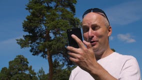Le mannen som använder mobiltelefonen för, stanna till video pratstund i sommar parkerar arkivfilmer Le mannen som använder mobiltelefonen för, stanna till video pratstund i sommar parkerar arkivfilmer