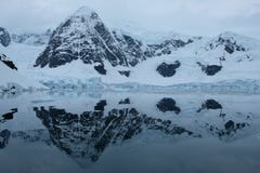 Le montagne ed i ghiacciai dell'Antartide riflettono nella baia blu dello specchio il giorno nuvoloso fotografia stock Le montagne ed i ghiacciai dell'Antartide riflettono nella baia blu dello specchio il giorno nuvoloso fotografia stock