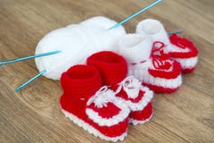 Le paia di bianco fatto a mano e di rosso hanno tricottato le pantofole e la palla del filato Immagini Stock Libere da Diritti Le paia di bianco fatto a mano e di rosso hanno tricottato le pantofole e la palla del filato Immagini Stock Libere da Diritti
