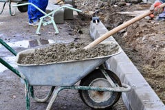 Le pale del lavoratore concrete da una carriola al bordo bloccano l'installazione immagine stock Le pale del lavoratore concrete da una carriola al bordo bloccano l'installazione immagine stock