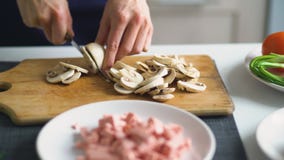 Le plan rapproché de la fille remet couper les champignons sur le conseil en bois pour la pizza dans la cuisine à la maison Photo libre de droits Le plan rapproché de la fille remet couper les champignons sur le conseil en bois pour la pizza dans la cuisine à la maison Photo libre de droits