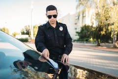 Le policier masculin dans l'uniforme écrit une amende sur la route photos stock Le policier masculin dans l'uniforme écrit une amende sur la route photos stock