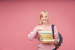 Le portrait d'une belle étudiante avec un sac à dos et d'une pile de livres dans des ses mains sourit au fond rose images stock Le portrait d'une belle étudiante avec un sac à dos et d'une pile de livres dans des ses mains sourit au fond rose images stock