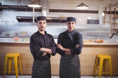 Le portrait des jeunes sûrs attendent le personnel dans l'uniforme noir se tenant avec des bras croisés au café images libres de droits Le portrait des jeunes sûrs attendent le personnel dans l'uniforme noir se tenant avec des bras croisés au café images libres de droits