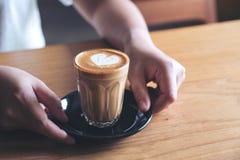 Le ` s de femme remet tenir et donner un verre de café chaud avec l'art de latte de coeur sur la table en bois de vintage Photos stock Le ` s de femme remet tenir et donner un verre de café chaud avec l'art de latte de coeur sur la table en bois de vintage Photos stock