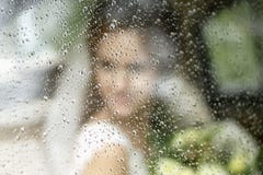 Le spose profilano in un vestito da sposa con un mazzo dei fiori attraverso vetro nelle gocce di pioggia immagine stock libera da diritti Le spose profilano in un vestito da sposa con un mazzo dei fiori attraverso vetro nelle gocce di pioggia immagine stock libera da diritti
