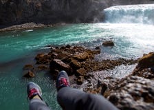 Le touriste s'assied sur une falaise près de la rivière, accrochant ses jambes vers le bas, v images stock Le touriste s'assied sur une falaise près de la rivière, accrochant ses jambes vers le bas, v images stock