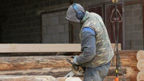 Le travailleur de la construction coupe la tronçonneuse en bois pour la future maison Masque protecteur et écouteurs sur la tête banque de vidéos Le travailleur de la construction coupe la tronçonneuse en bois pour la future maison Masque protecteur et écouteurs sur la tête banque de vidéos
