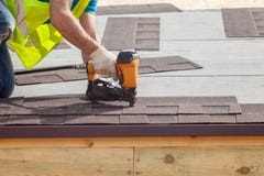 Le travailleur de la construction mettant les bardeaux de toiture d'asphalte avec le clou lancent sur une nouvelle maison de cadr photos stock Le travailleur de la construction mettant les bardeaux de toiture d'asphalte avec le clou lancent sur une nouvelle maison de cadr photos stock