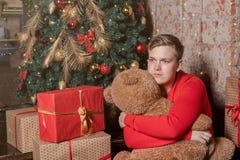 Le type beau étreint l'ours se reposant sous l'arbre entouré par des boîtes de cadeaux Noël et cadeaux photos stock Le type beau étreint l'ours se reposant sous l'arbre entouré par des boîtes de cadeaux Noël et cadeaux photos stock