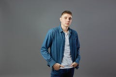 Le type habillé dans un T-shirt blanc, les jeans et la chemise de jeans tient ses mains dans des poches dans le studio sur le fon photo libre de droits Le type habillé dans un T-shirt blanc, les jeans et la chemise de jeans tient ses mains dans des poches dans le studio sur le fon photo libre de droits