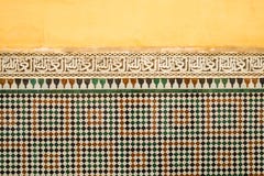 Le vieux jaune marocain coloré a peint le mur avec une bande de la calligraphie islamique au-dessus du tilework de zellige images stock Le vieux jaune marocain coloré a peint le mur avec une bande de la calligraphie islamique au-dessus du tilework de zellige images stock