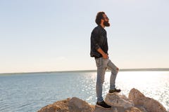 Le voyageur se tient sur une roche contre d'une belle les vagues paisibles mer, un garçon barbu élégant de hippie posant près d'u photos libres de droits Le voyageur se tient sur une roche contre d'une belle les vagues paisibles mer, un garçon barbu élégant de hippie posant près d'u photos libres de droits