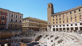 LECCE, ITÁLIA - 2 DE AGOSTO DE 2017: Anfiteatro romano com os palácios do Sedile e do delle Assicurazioni de INA Istituto Naziona imagens de stock royalty free LECCE, ITÁLIA - 2 DE AGOSTO DE 2017: Anfiteatro romano com os palácios do Sedile e do delle Assicurazioni de INA Istituto Naziona imagens de stock royalty free