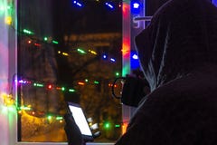 ledsen man i en huv med en smartphone i en suddig bokeh, på bakgrunden av fönstret som dekoreras med girlander med ett tomt arkivfoton ledsen man i en huv med en smartphone i en suddig bokeh, på bakgrunden av fönstret som dekoreras med girlander med ett tomt arkivfoton