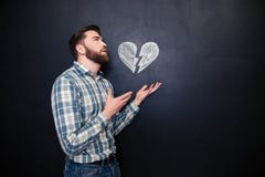 Ledset romantiskt dragen bruten hjärta för man innehav över svart tavlabakgrund arkivfoto Ledset romantiskt dragen bruten hjärta för man innehav över svart tavlabakgrund arkivfoto