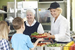 Leerlingen in Schoolcafetaria die Gediende Lunch door Dinerdames zijn stock fotografie Leerlingen in Schoolcafetaria die Gediende Lunch door Dinerdames zijn stock fotografie