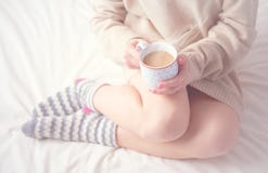 Legs of girl warm woolen socks and cup of coffee warming, winter morning in bed