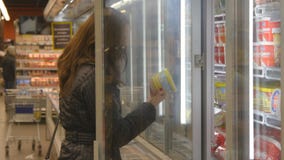 Leiteria de compra da jovem mulher ou mantimentos refrigerados no supermercado na porta de vidro de abertura refrigerada da seção filme Leiteria de compra da jovem mulher ou mantimentos refrigerados no supermercado na porta de vidro de abertura refrigerada da seção filme