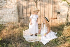 Les belles soeurs blondes de fille dans des robes et des chapeaux de paille de blanc rient et mangent des pommes dans la campagne photographie stock Les belles soeurs blondes de fille dans des robes et des chapeaux de paille de blanc rient et mangent des pommes dans la campagne photographie stock